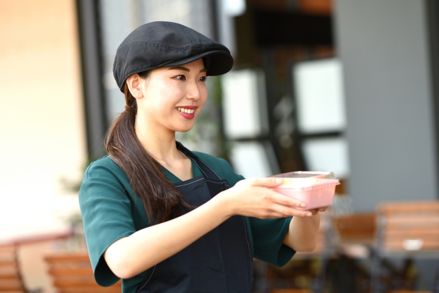 にっこり微笑んで手渡すTシャツ姿の店舗スタッフ