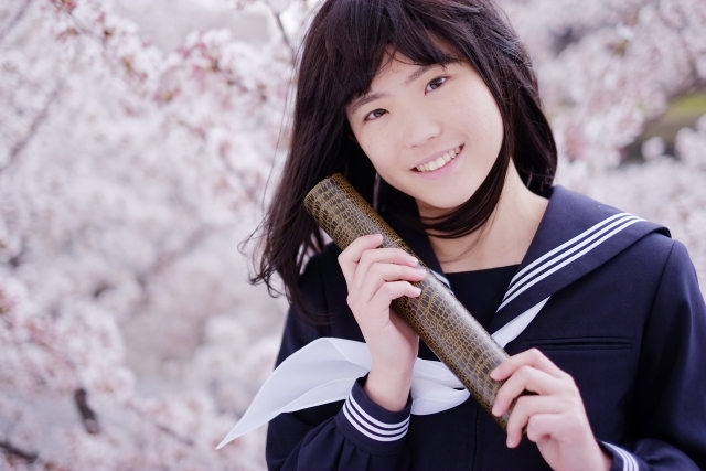 満開の桜をバックに微笑む卒業式の女子学生